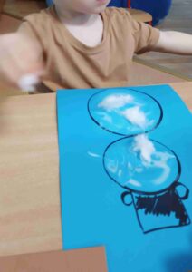 Dzieci wyklejają bałwana watą.