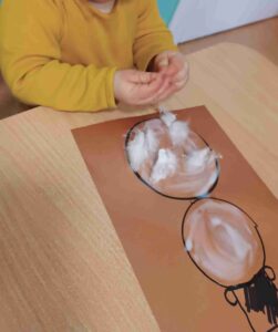 Dzieci wyklejają bałwana watą.