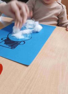 Dzieci wyklejają bałwana watą.