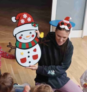 Młoda dziewczyna pokazuje dzieciom bałwana naklejonego na kartonie.