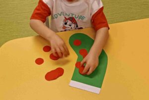 Dziecko wykleja zieloną skarpetę z papieru czerwonymi kropkami