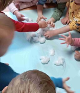 Dzieci wyklejają bałwana watą.