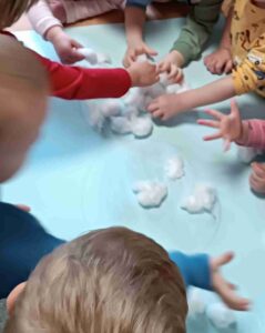 Dzieci wyklejają bałwana watą.