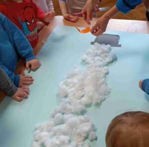Dzieci wyklejają bałwana watą.